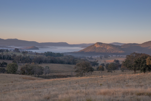 An early morning country scene with fields, mist and a granite outcrop - Australian Stock Image