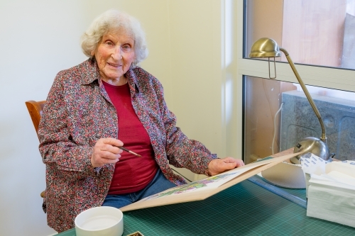 An elderly lady artist sitting at her work with a brush in her hand - Australian Stock Image