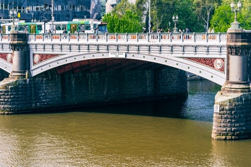 An electric tram crossing an historic arched bridge over a river - Australian Stock Image