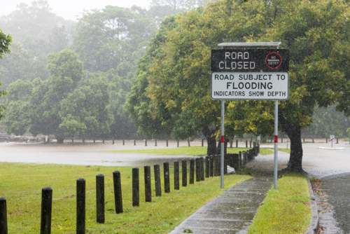 An electronic street sign saying road closed due to flooding with water in background - Australian Stock Image