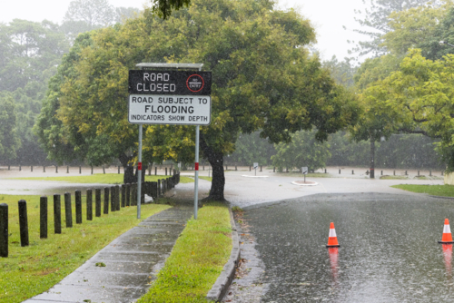 An electronic street sign saying road closed due to flooding with water in background - Australian Stock Image