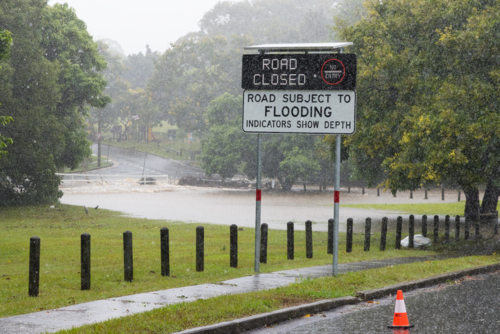 An electronic street sign saying road closed due to flooding with water in background - Australian Stock Image