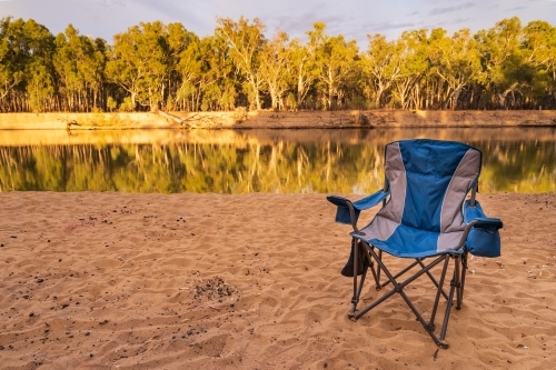An empty camp chair sitting on a sandy river bank - Australian Stock Image