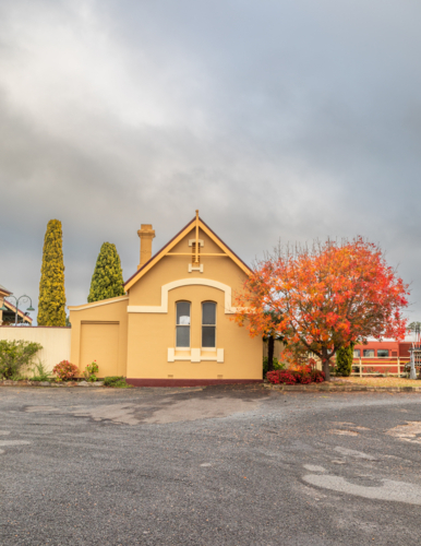 An old country railway building with a tree with autumn foliage - Australian Stock Image