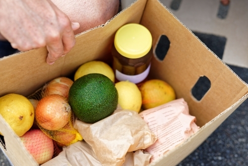 An open box of fresh produce containing honey, avocado, lemons and onions