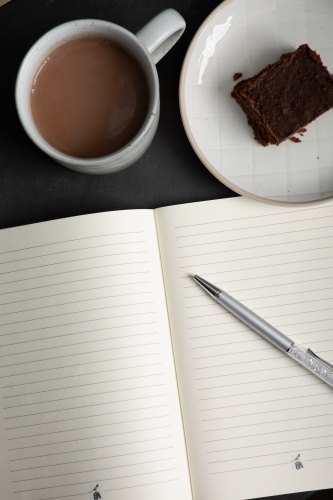 an open notebook with a mug of hot chocolate and piece of chocolate brownie