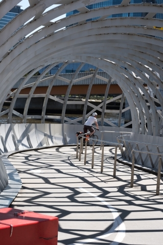 Anonymous cyclist riding through The Net Bridge in Melbourne's Docklands - Australian Stock Image