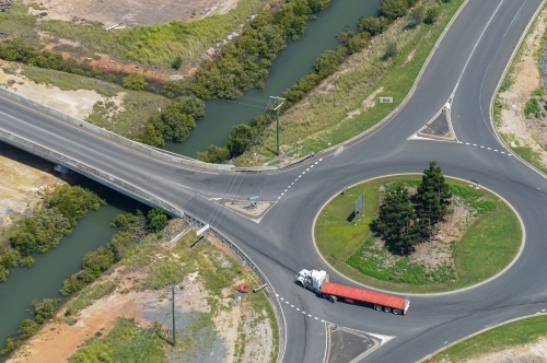 Articulated semi trailer truck going around a roundabout next to a bridge over a creek. - Australian Stock Image