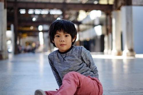 asian boy staring at camera, and sitting on a warehouse floor