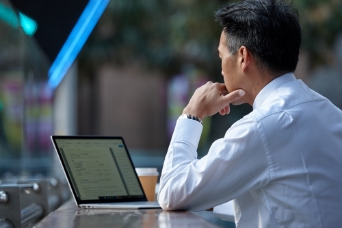 Asian businessman working on laptop in a cafe in the city - Australian Stock Image