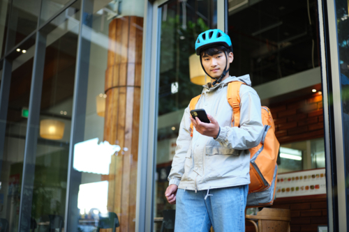 Asian delivery guy walking out of the restaurant while on his phone. - Australian Stock Image