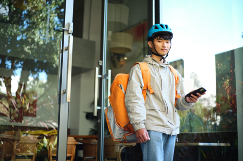 Asian delivery guy walking out of the restaurant while on his phone - Australian Stock Image