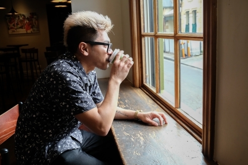 Asian man drinking coffee by the window - Australian Stock Image