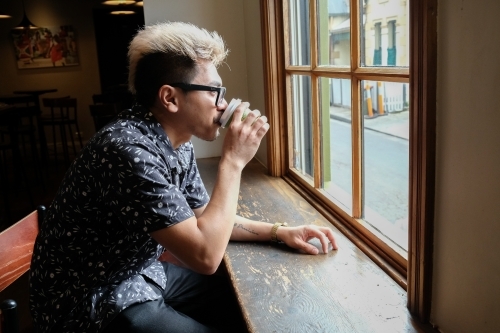 Asian man drinking coffee by the window