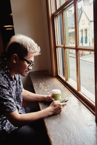 Asian man holding coffee cup and using mobile phone - Australian Stock Image