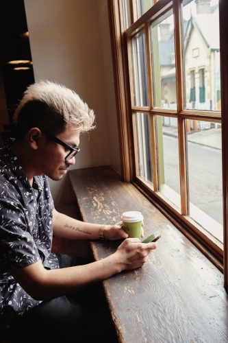 Asian man holding coffee cup and using mobile phone