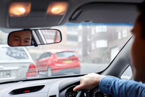 Asian man looking in rear view mirror whilst driving in car - Australian Stock Image