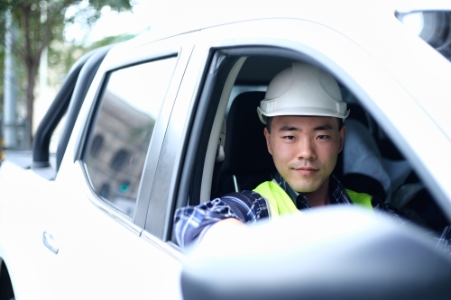 Asian man wearing hard hat in car