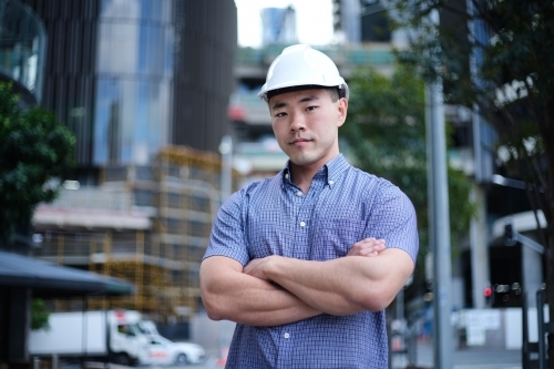Asian man wearing hard hat with city background - Australian Stock Image