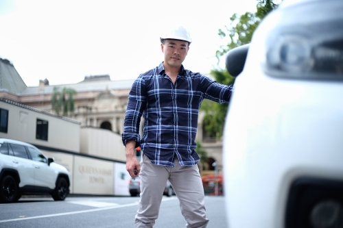 Asian man with hard hat getting into car - Australian Stock Image