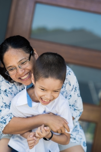 Asian mum hugs her son goodbye at the front door of her home on his first day of school - Australian Stock Image