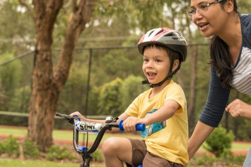 Asian mum teaching her mixed race boy to ride a bike - Australian Stock Image