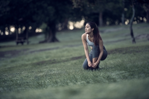 Asian runner tying shoelaces in park during morning exercise - Australian Stock Image