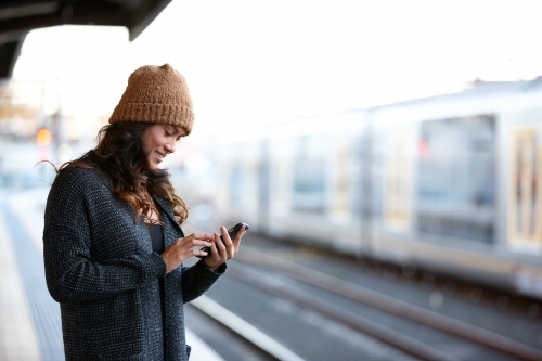 Asian woman checking messages at train station with mobile phone - Australian Stock Image