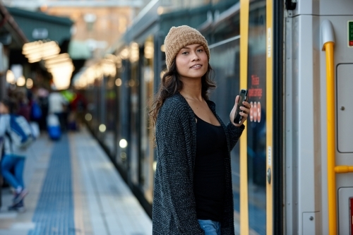 Asian woman getting on train with mobile phone - Australian Stock Image