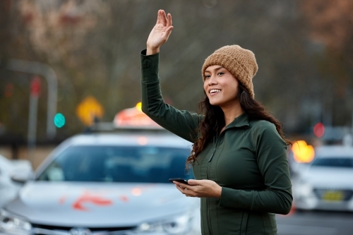 Asian woman hailing taxi with mobile phone - Australian Stock Image