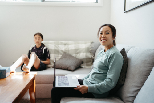 Asian woman holding a laptop sitting on the couch with daughter - Australian Stock Image