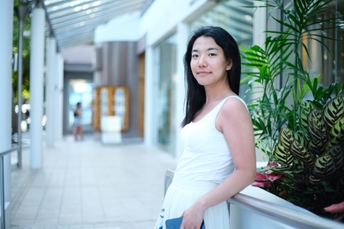 Asian woman holding a phone while leaning against the metal railing along the walkway. - Australian Stock Image