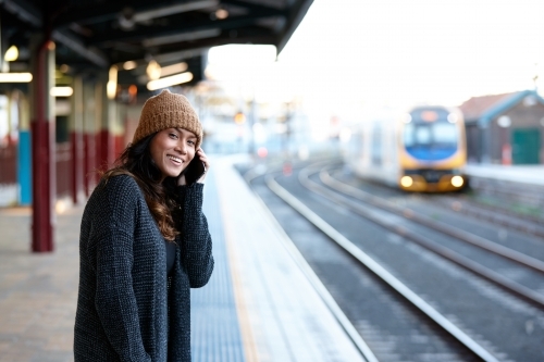 Asian woman laughing whilst waiting at train station with mobile phone - Australian Stock Image