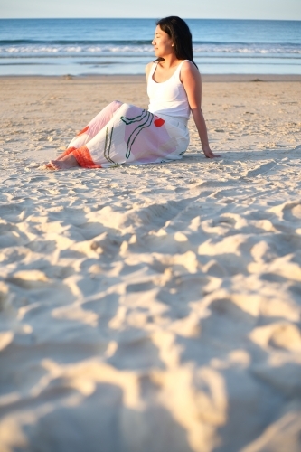Asian woman sitting on the sand on the beach. - Australian Stock Image