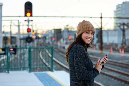 Asian woman smiling whilst waiting at train station - Australian Stock Image