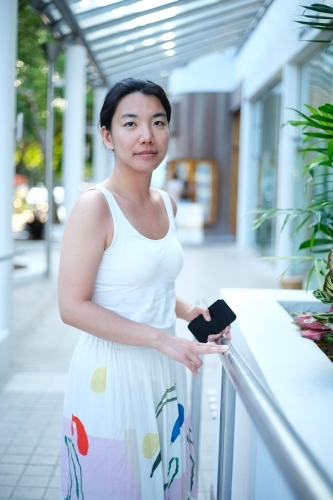 Asian woman standing along the walkway while holding her phone - Australian Stock Image