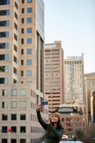 Asian woman taking photo with mobile phone in city - Australian Stock Image