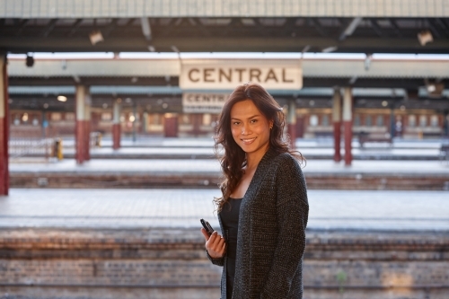 Asian woman waiting at train station with mobile phone - Australian Stock Image