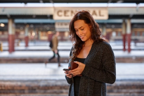 Asian woman waiting at train station with mobile phone - Australian Stock Image