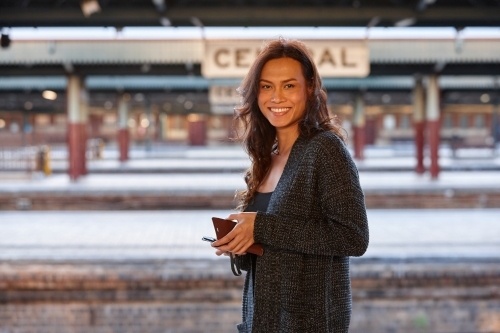 Asian woman waiting at train station with mobile phone - Australian Stock Image