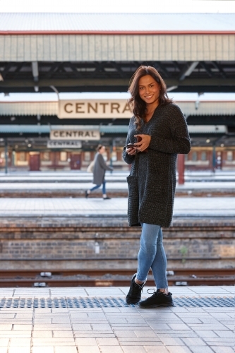 Asian woman waiting at train station with mobile phone - Australian Stock Image