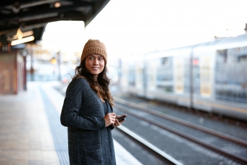 Asian woman waiting at train station with mobile phone - Australian Stock Image