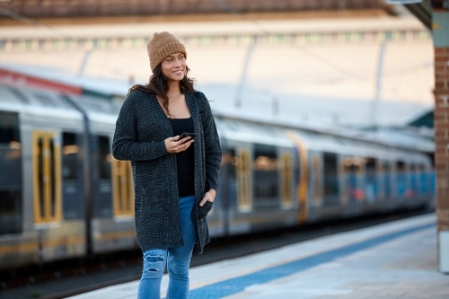 Asian woman waiting at train station with mobile phone - Australian Stock Image