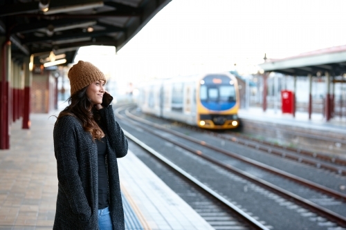 Asian woman waiting for train whilst talking on mobile phone - Australian Stock Image