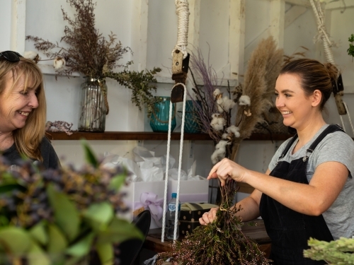 Attractive female florist happily interacting with older lady client while preparing flowers. - Australian Stock Image