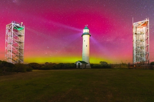Aurora Australis filling the night sky over a tall lighthouse and nearby navigation towers - Australian Stock Image