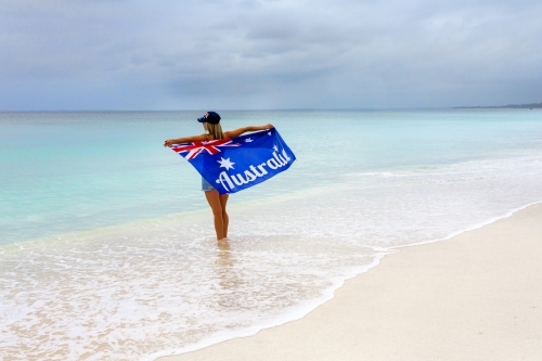 Aussie culture. A woman stands on a stunning beach holding proudly the Australian Flag - Australian Stock Image