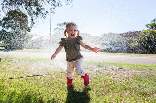 Aussie kid running through sprinkler in bright sunlight - Australian Stock Image