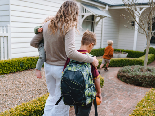 Aussie mum carrying toddler boy while walking with older son from school towards home - Australian Stock Image