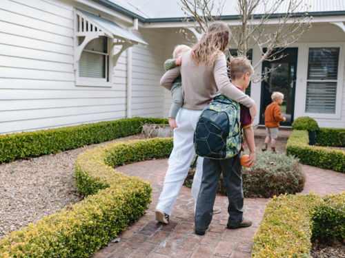 Aussie mum carrying toddler boy while walking with older son from school towards home - Australian Stock Image